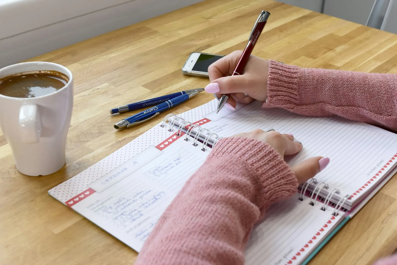 A hand writing in a notebook beside morning coffee A hand writing in a notebook beside morning coffee